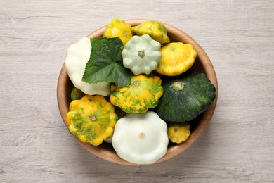 Fresh ripe pattypan squashes in bowl on light wooden table, top view