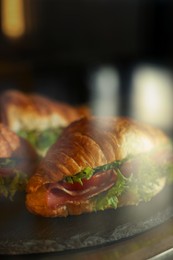 Photo of Showcase with yummy croissant sandwiches in cafe, closeup