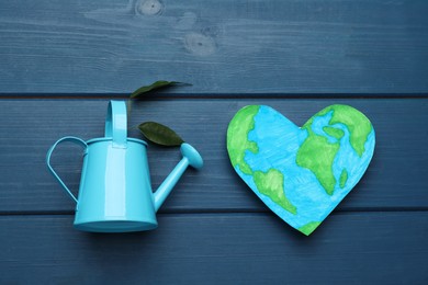 Happy Earth Day. Heart shaped plasticine planet and watering can with plant on blue wooden table, flat lay