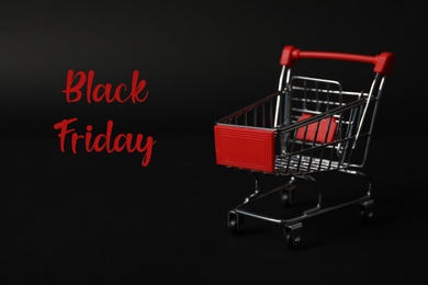 Phrase Black Friday and toy shopping cart on dark background