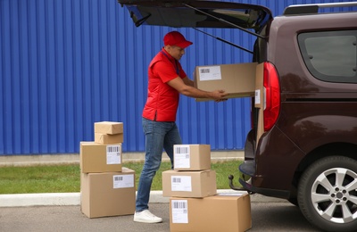 Courier loading packages in car trunk outdoors