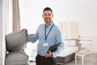 Photo of Happy salesman showing cushions in mattress store