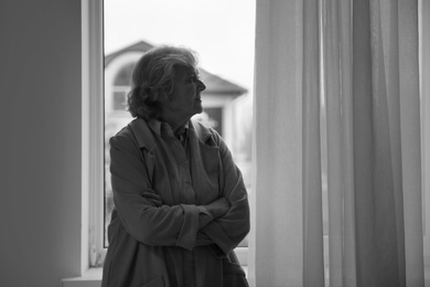 Portrait of elderly woman near window indoors, space for text. Black and white effect