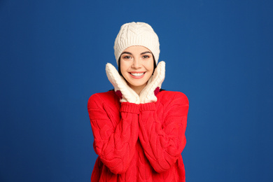 Young woman wearing warm sweater, mittens and hat on blue background. Winter season
