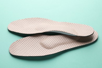 Beige comfortable orthopedic insoles on turquoise background, closeup