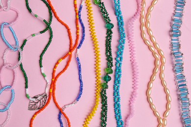 Beautiful handmade beaded necklaces on pink background, flat lay