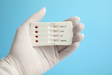 Doctor holding disposable express test for hepatitis on light blue background, closeup