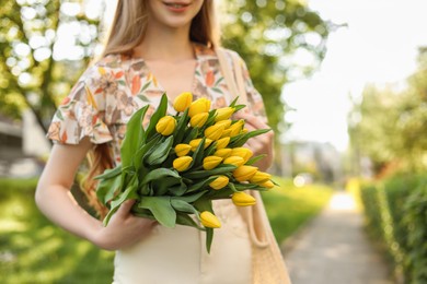 Teenage girl with bouquet of yellow tulips in park on sunny day, closeup