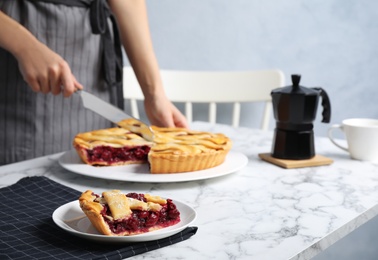 Closeup view of woman cutting tasty cherry pie at white marble table, focus on plate with slice