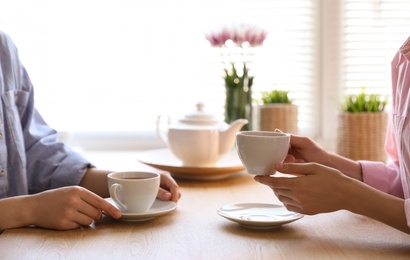 Women with cups of tea at table near window indoors, closeup