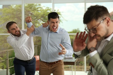 Man interrupting colleagues fight at work in office