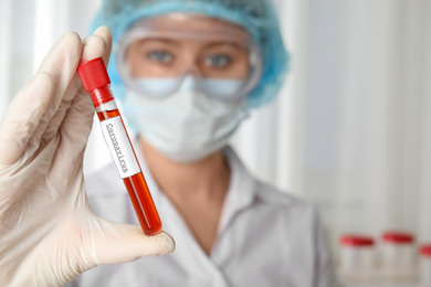 Scientist holding test tube with blood sample and label CORONA VIRUS in laboratory, focus on hand