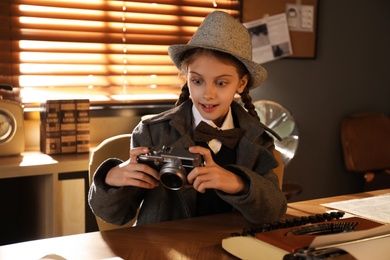 Cute little detective with camera at table in office