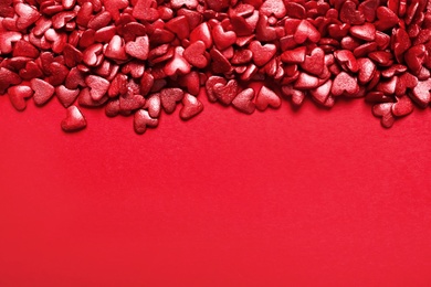 Bright heart shaped sprinkles on red background, view from above. Space for text