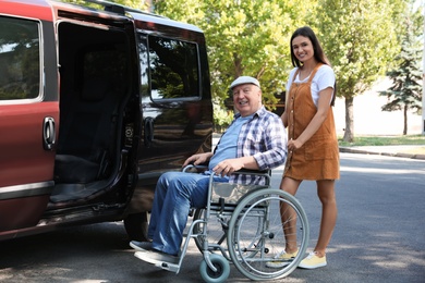 Young woman helping senior man in wheelchair to get into van outdoors