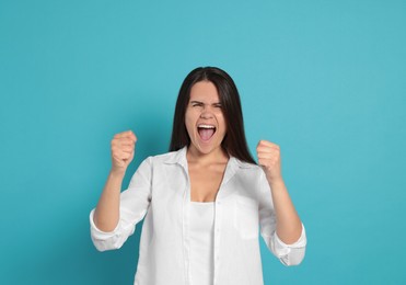 Aggressive young woman shouting on turquoise background