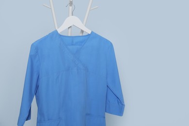 Photo of Blue medical uniform hanging on rack against light grey background. Space for text