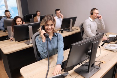 Young call center operator talking on phone and her colleagues working in modern office
