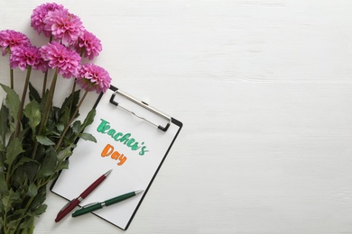 Beautiful flowers and clipboard with words TEACHER'S DAY on white wooden background, flat lay. Space for text