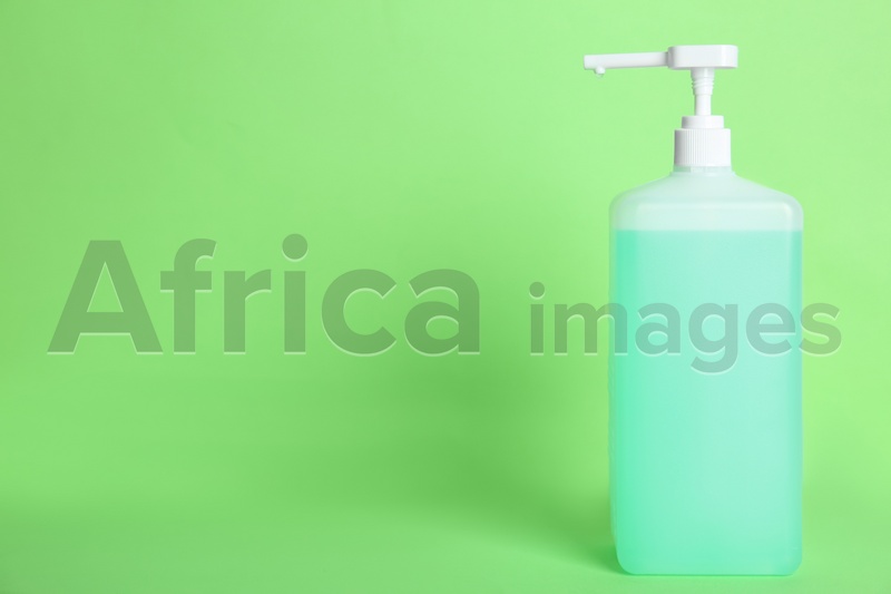 Dispenser bottle with antiseptic gel on green background. Space for text