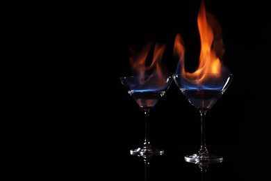 Cocktail glasses with flaming vodka on black background, space for text