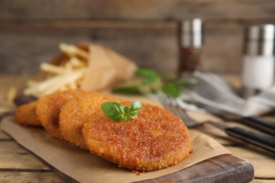 Delicious fried breaded cutlets with basil on wooden table, closeup