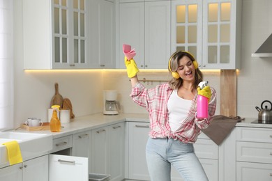 Photo of Beautiful young woman with headphones singing while cleaning kitchen