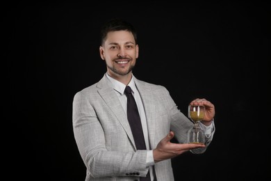 Happy businessman holding hourglass on black background. Time management