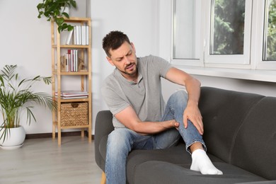 Man suffering from pain in leg on sofa at home