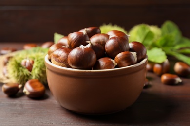 Fresh sweet edible chestnuts on brown wooden table, closeup