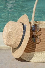 Stylish bag, sunglasses and hat near outdoor swimming pool on sunny day. Beach accessories