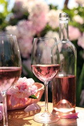 Photo of Bottle and glasses of rose wine near beautiful peonies on wooden table in garden