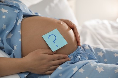 Pregnant woman with sticky note on belly indoors, closeup. Choosing baby name