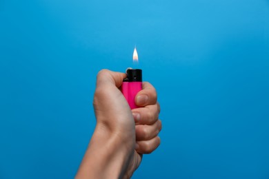Woman holding pink lighter on light blue background, closeup