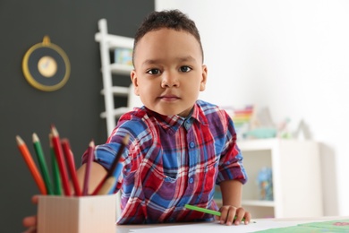 Cute little African-American child drawing at table in kindergarten. Indoor activity