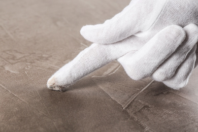 Person in white glove checking cleanliness of beige stone table, closeup