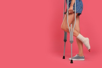 Young woman with injured leg using axillary crutches on pink background, closeup. space for text