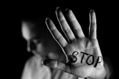 Image of Woman with word Stop written on hand against black background, closeup. Domestic violence concept