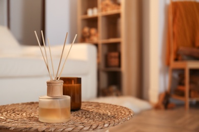 Aromatic reed air freshener and candle on wicker tray in room. Space for text