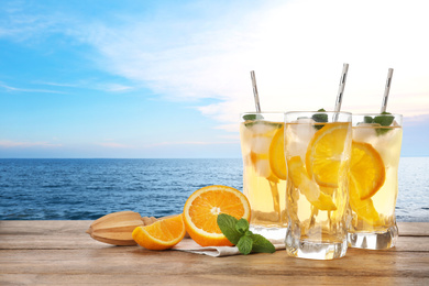 Tasty refreshing drink on wooden table against sea
