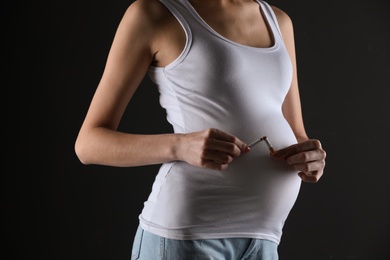 Young pregnant woman breaking cigarette on black background, closeup