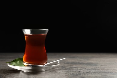 Glass with traditional Turkish tea on grey table against black background, space for text