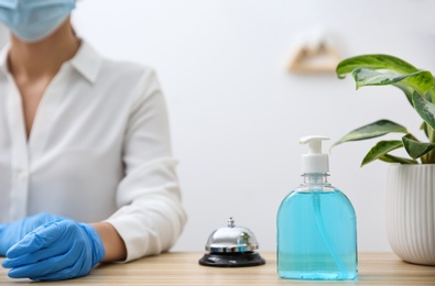 Receptionist at countertop in hotel, focus on dispenser bottle with antiseptic gel and service bell