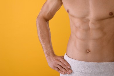 Shirtless man with slim body and towel wrapped around his hips on yellow background, closeup