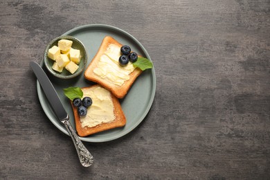 Photo of Delicious toasts served with butter and blueberries on grey wooden table, top view. Space for text