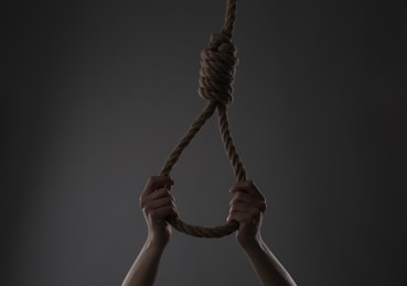 Woman holding rope noose on grey background, closeup