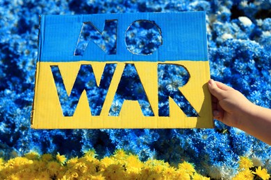 Woman holding poster in colors of Ukrainian flag with words No War and beautiful blue and yellow flowers on background, closeup