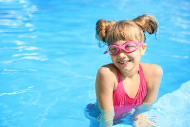 Happy girl wearing goggles in swimming pool. Space for text