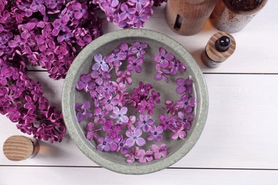 Photo of Cosmetic products and lilac flowers on white wooden table, flat lay