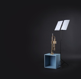 Trumpet and note stand with music sheets on black background. Space for text